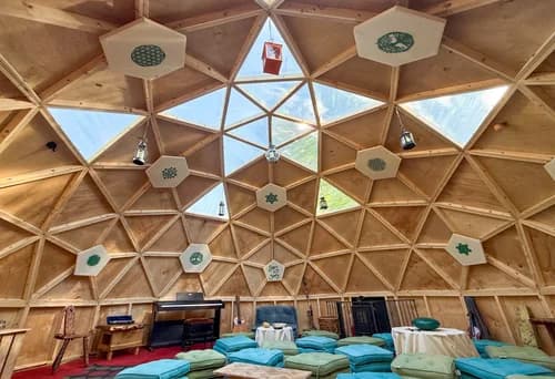 Inside the geodesic dome with sacred geometry panels, cushions, and natural light flooding through the star ceiling
